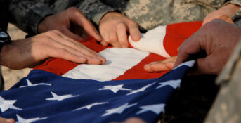 Veterans lay their hands upon a folded American flag