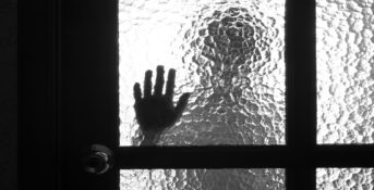 The silhouette of a person with their hand pressed against the glass